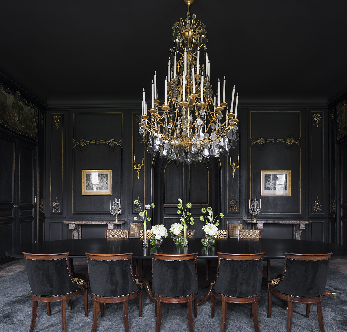 A dark dining room with a chandelier hanging over the table 