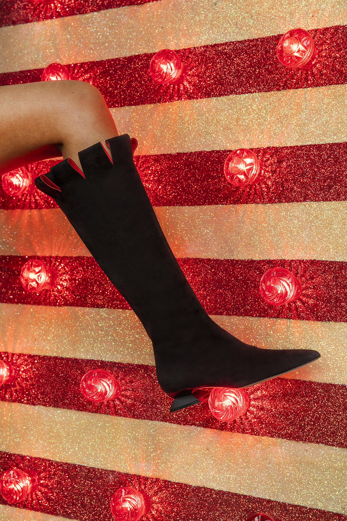 Leg in suede black boot against a background of white and red stripes and lights 