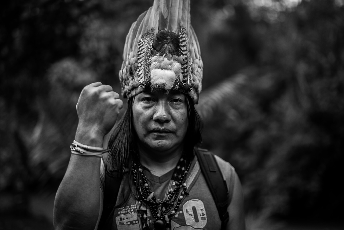 A Native American with a feather har holding his fist up in a black and white photo